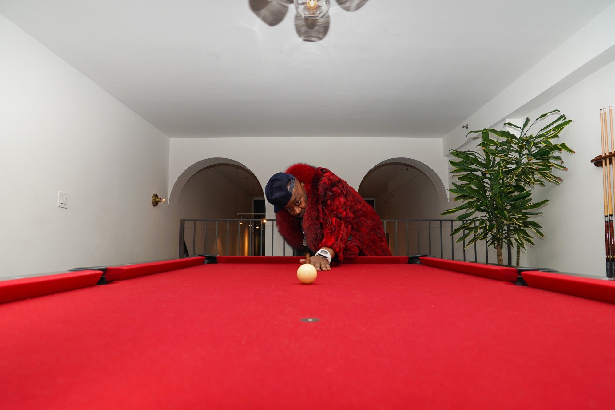 Ghostface Killah in a red fur coat lining up a shot across a red pool table