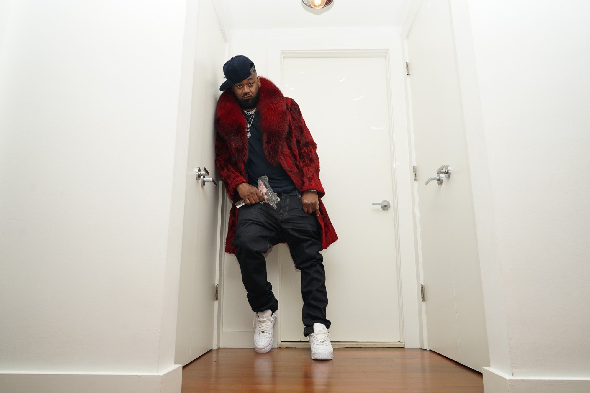 Ghostface Killah leaning in a white hallway in a red fur coat and white sneakers